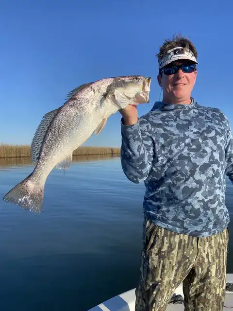 Angler in a visor holding up his catch over calm water near Venice, Louisiana