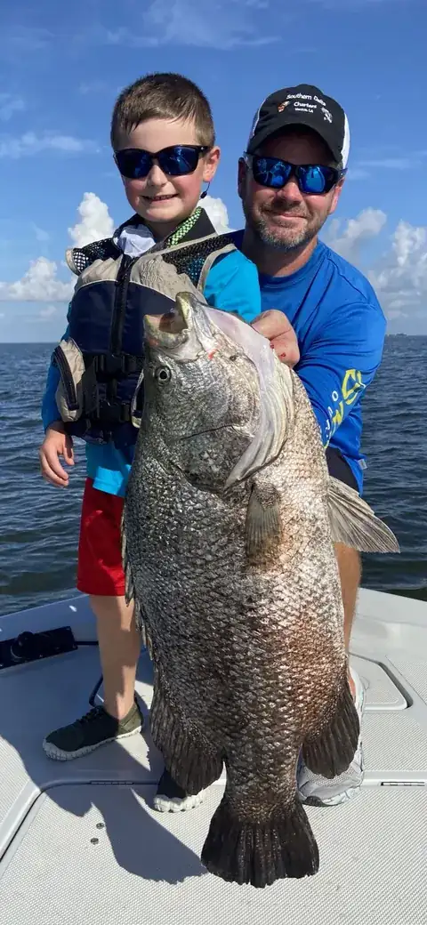 A young angler and an adult holding up a large black drum on the boat near Venice, Louisiana