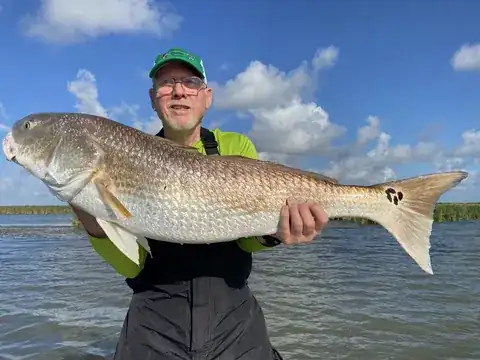 Angler in a green cap holding a bull redfish under a sky of scattered clouds near Venice, Louisiana