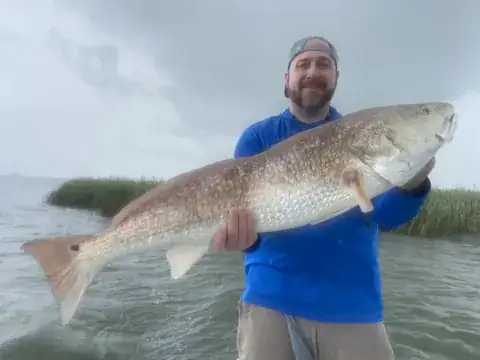 Angler holding a bull redfish under a stormy sky beside the marsh near Venice, Louisiana
