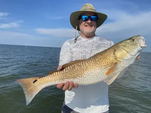 Angler in a sun hat holding a bull redfish over open water near Venice, Louisiana