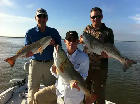 Three anglers holding bull redfish on the deck of a Southern Delta Charters boat