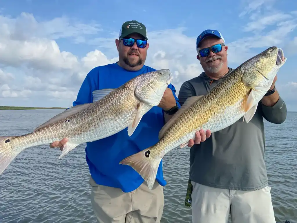 Two anglers in Southern Delta Charters caps each holding a bull redfish on open water