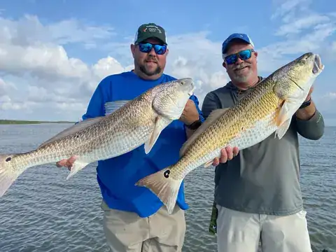 Two anglers in Southern Delta Charters caps each holding a bull redfish on open water near Venice, Louisiana