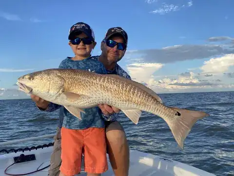 A young angler and an adult holding a bull redfish over open water near Venice, Louisiana