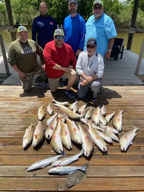 Six anglers behind a catch of redfish laid out on the dock in Venice, Louisiana
