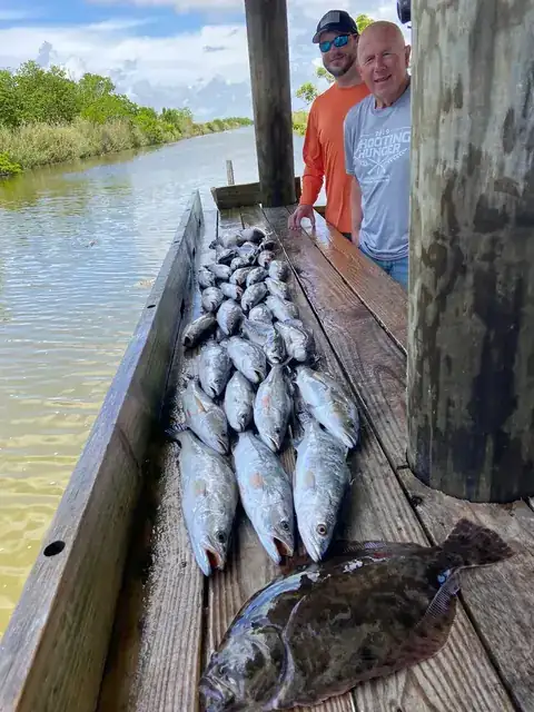 Two anglers beside a catch of speckled trout and a flounder on the cleaning dock in Venice, Louisiana