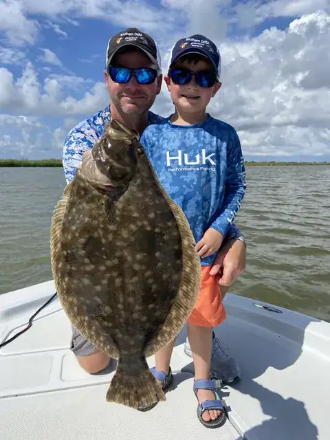 A young angler and an adult holding up a large flounder on the boat near Venice, Louisiana