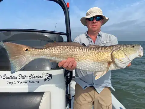 Angler holding a redfish beside the console lettered Southern Delta Charters, Capt. Kasye Bourn