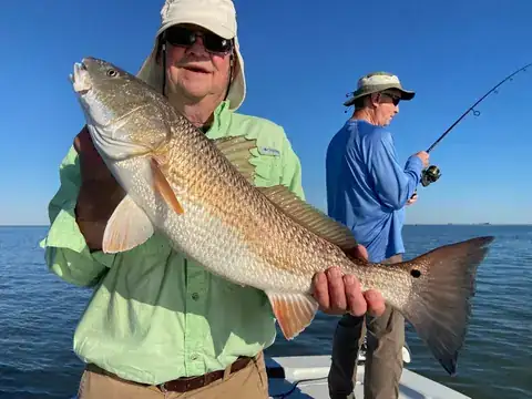 Angler in a green shirt holding a redfish while another fishes behind him near Venice, Louisiana