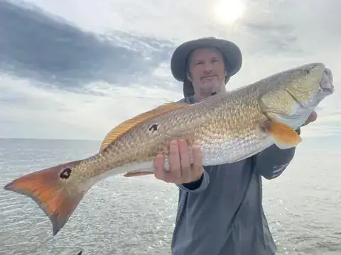 Angler in a sun hat holding a redfish out toward the camera near Venice, Louisiana