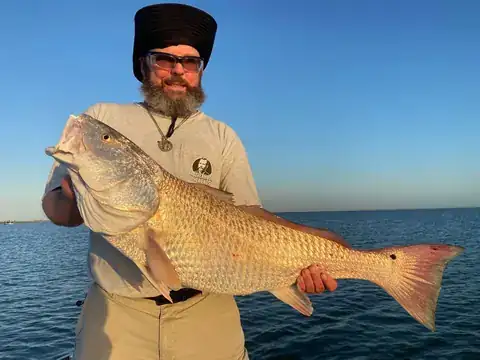 Bearded angler holding a large redfish in low evening light near Venice, Louisiana