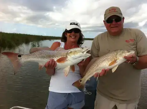 Two anglers each holding a redfish in front of delta marsh grass