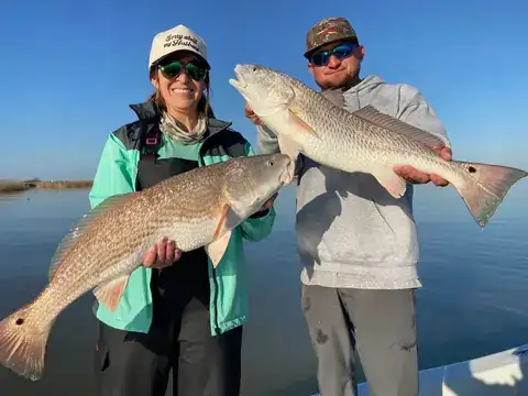 Two anglers each holding a redfish on the boat