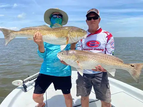Two anglers standing on the bow, each holding a redfish
