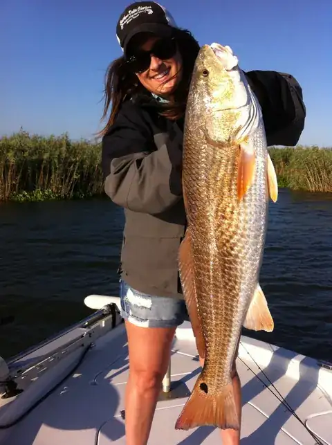 Angler in a Southern Delta Charters cap holding a redfish upright on the bow in front of marsh cane