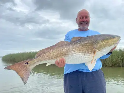 Angler holding a large redfish with delta marsh grass behind him near Venice, Louisiana