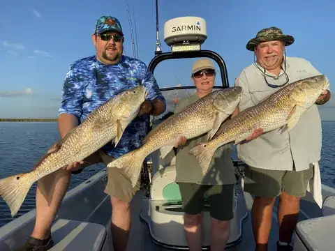 Three anglers each holding a redfish on the boat in evening light near Venice, Louisiana