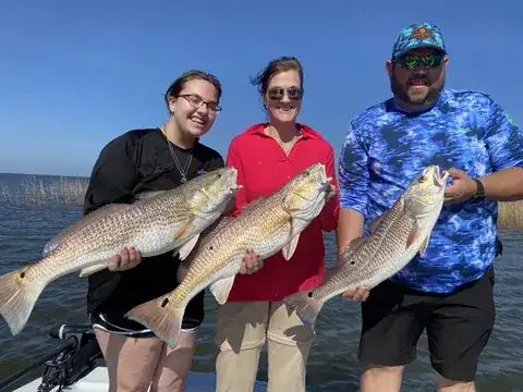 Three anglers on the boat each holding a redfish near Venice, Louisiana