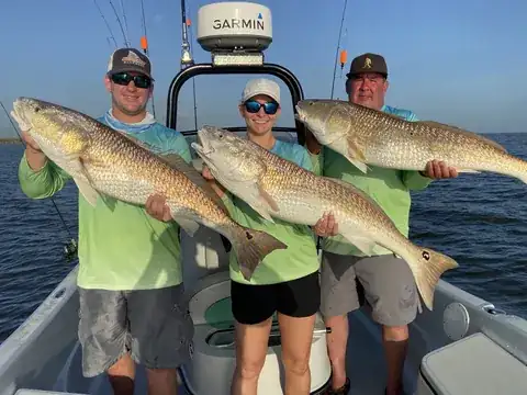 Three anglers each holding a redfish in front of the boat's console near Venice, Louisiana