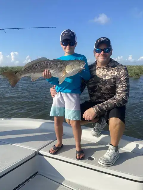 A young angler holding a redfish on the bow beside a seated adult near Venice, Louisiana