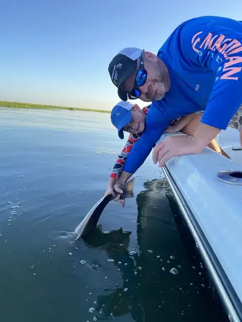 An adult and a young angler leaning over the gunwale to release a fish