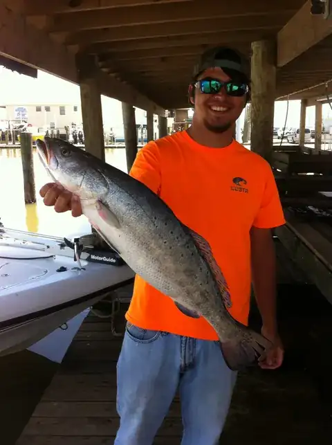 Angler in an orange shirt holding a speckled trout at the dock in Venice, Louisiana