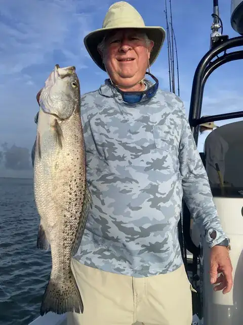 Angler in a sun hat holding up a speckled trout beside the boat's console near Venice, Louisiana