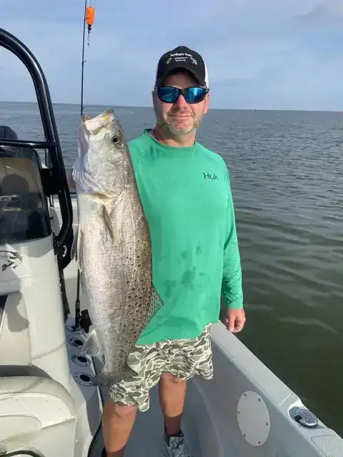 Angler in a green shirt holding up a large speckled trout beside the boat's console near Venice, Louisiana